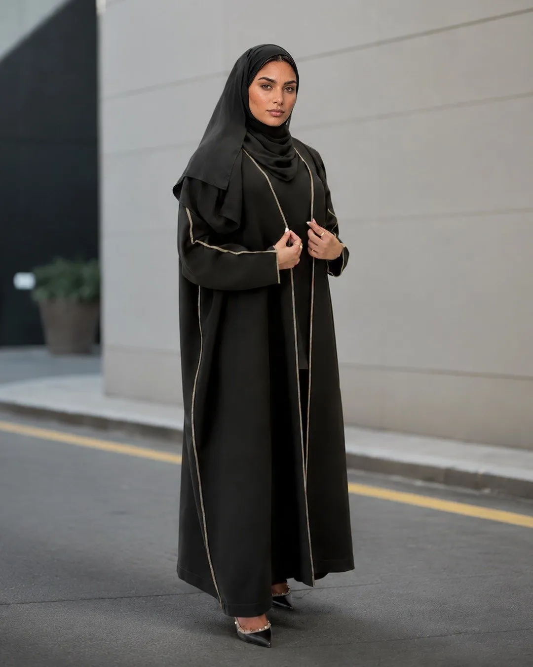 Model in a black abaya with fine gold-tone piping standing on a street