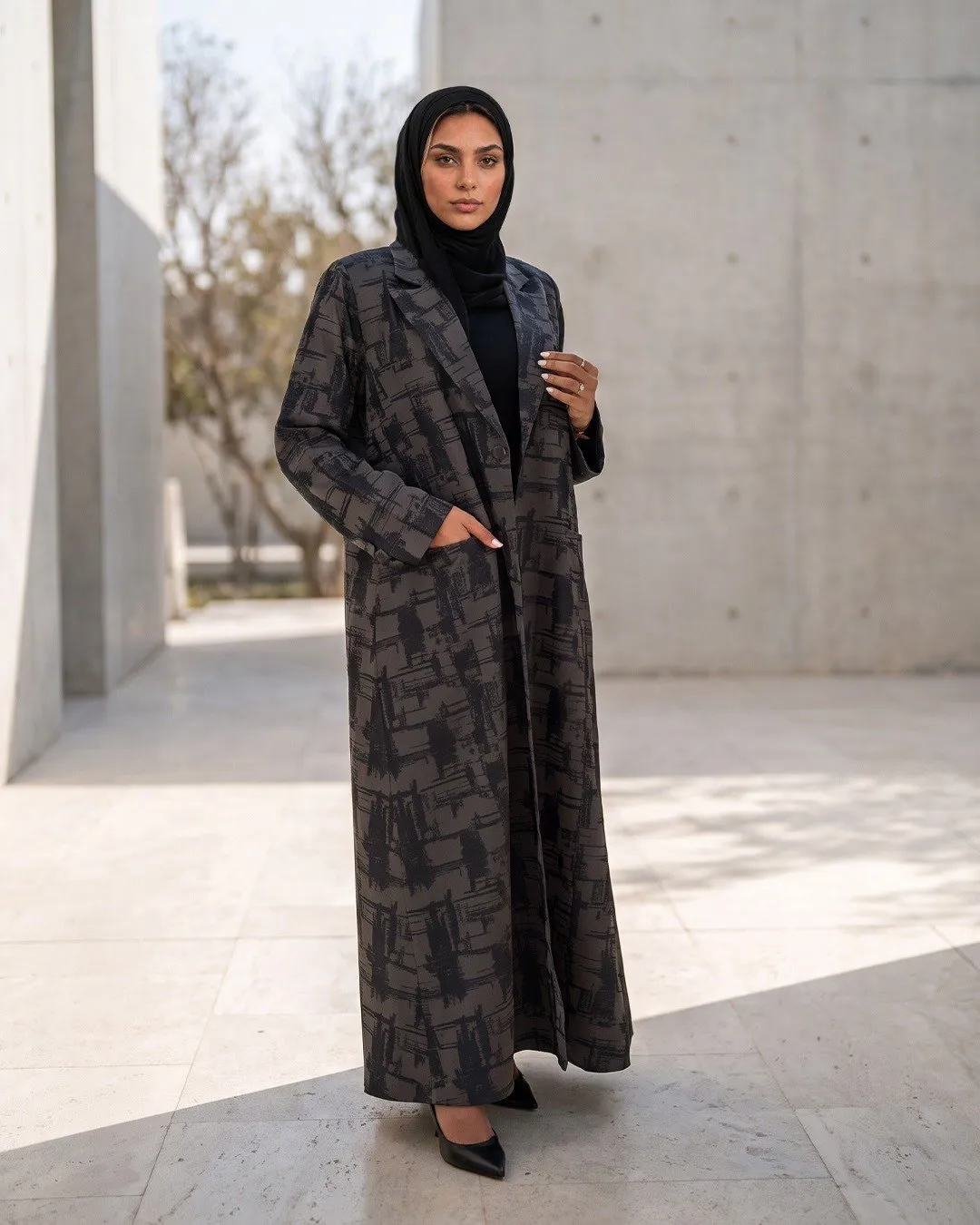 Model in a charcoal brushstroke print coat abaya in a concrete courtyard