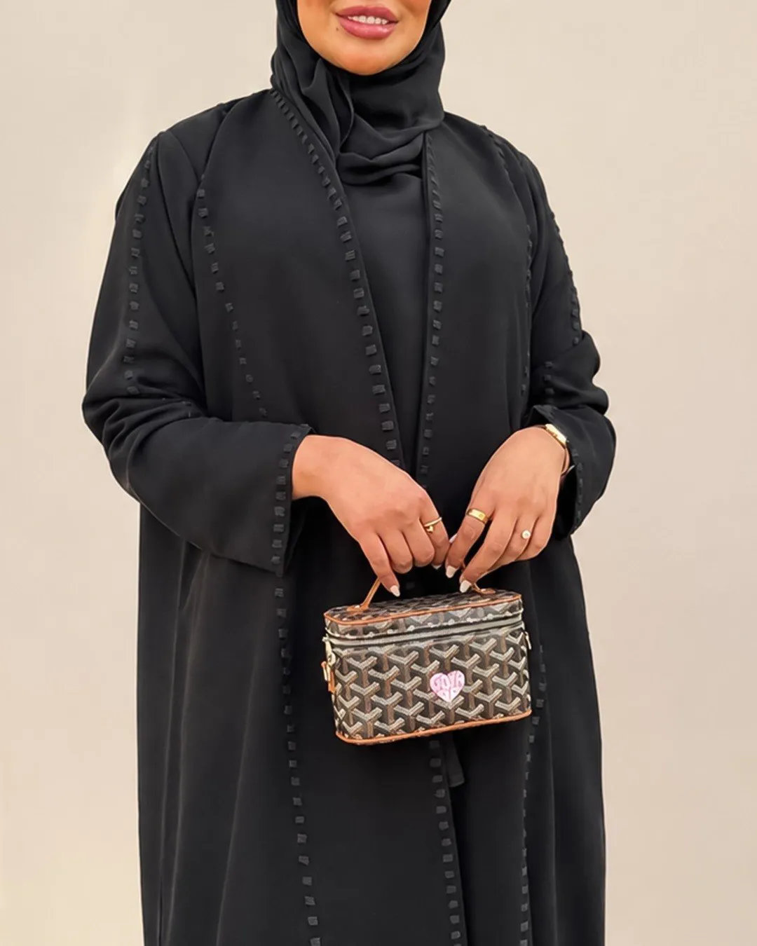 Model in a black abaya with raised stitch lines holding a small bag